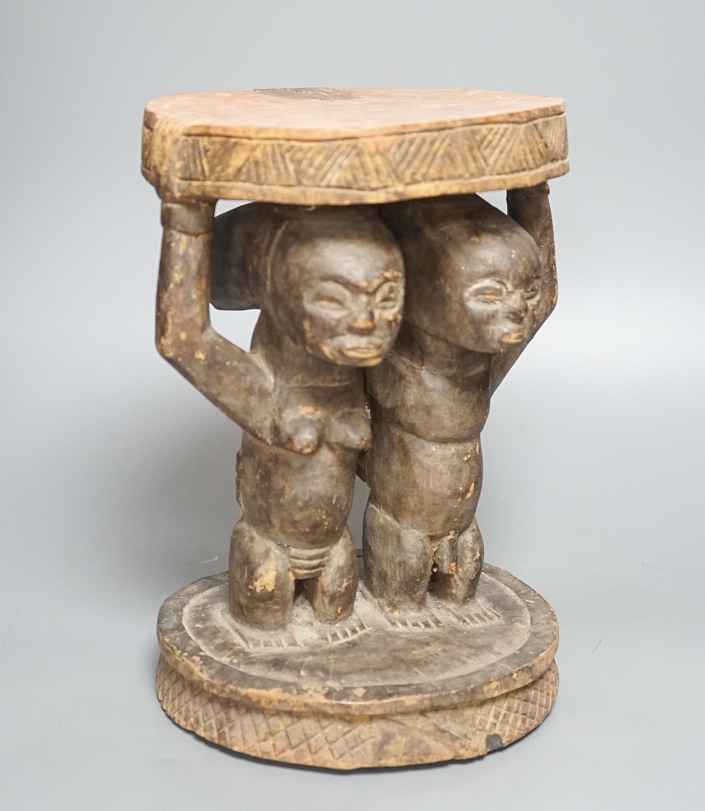 A Yoruba carved wood stool, modelled with male and female figures 27cm